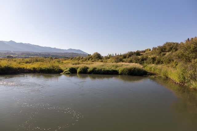 A calm river flows through a lush, green landscape with distant mountains under a clear blue sky.