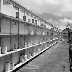 A long aisle between rows of marble crypts in a cemetery, with niches holding urns and inscribed plaques.