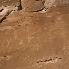 An ancient rock formation bears petroglyphs that depict various animals, including what appear to be deer and other creatures.