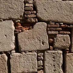 A close-up view of a wall constructed from large, irregular stone blocks, with smaller stones and bricks filling the gaps between them.