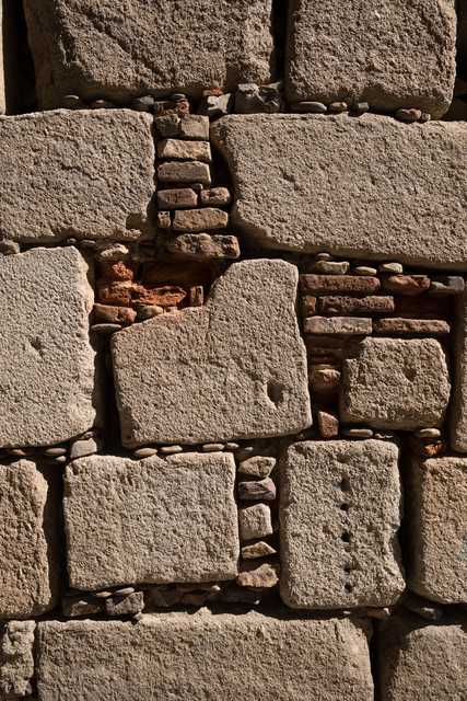 A close-up view of a wall constructed from large, irregular stone blocks, with smaller stones and bricks filling the gaps between them.