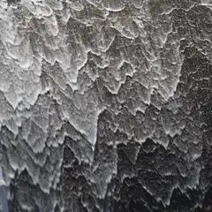 Water cascades over a dark, textured surface, creating a pattern of white, foamy ripples and splashes.