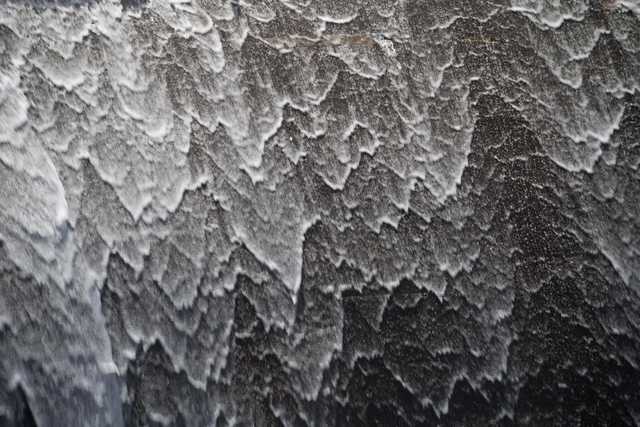 Water cascades over a dark, textured surface, creating a pattern of white, foamy ripples and splashes.