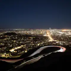 An aerial view of a city at night features a highway with light trails from cars traveling along it.