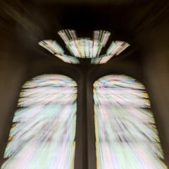 A zoom-burst effect captures arched stained-glass windows, their colors streaking outward from a central point in a dark interior.