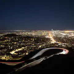 An aerial view of a city at night features a highway with light trails from cars traveling along it.
