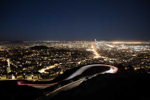 An aerial view of a city at night features a highway with light trails from cars traveling along it.