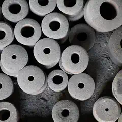 A collection of dusty gray, cylindrical objects with central holes, arranged in a disorganized pile.