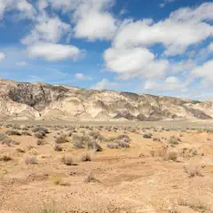 A desert landscape with rugged mountains and sparse vegetation under a partly cloudy sky.