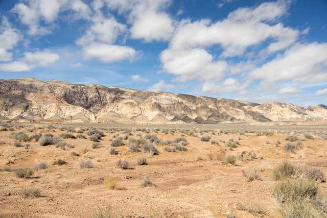 A desert landscape with rugged mountains and sparse vegetation under a partly cloudy sky.