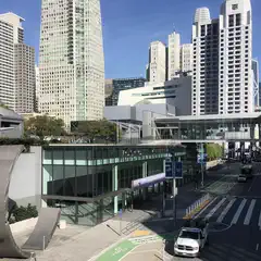 A large building with a glass facade is situated in front of a cluster of tall skyscrapers.
