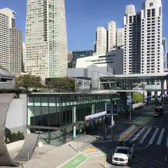 A large building with a glass facade is situated in front of a cluster of tall skyscrapers.