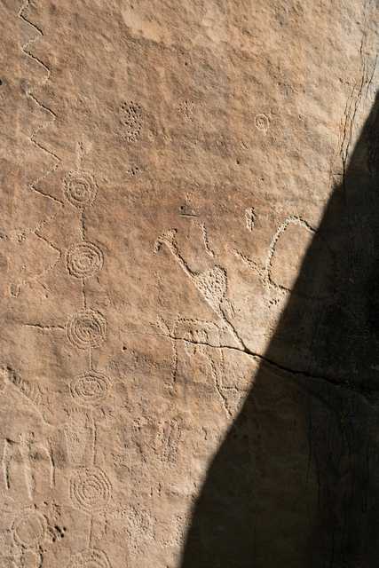 An ancient rock surface features various petroglyphs, including spirals, zigzags, and animal figures.
