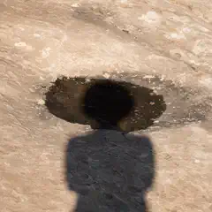 A rocky surface with an oval shape on the ground and a shadow of a person in front of it.
