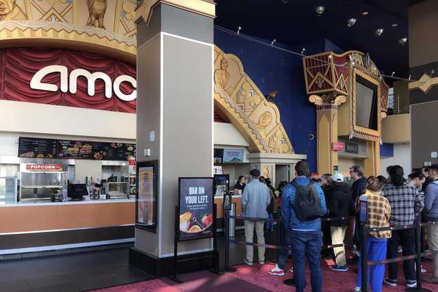 A group of people standing in line at a concession counter inside a movie theater.
