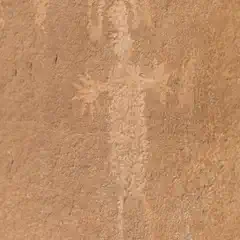 A petroglyph on a reddish-brown rock face depicts a stylized human figure with an elongated body.