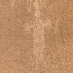 A petroglyph on a reddish-brown rock face depicts a stylized human figure with an elongated body.