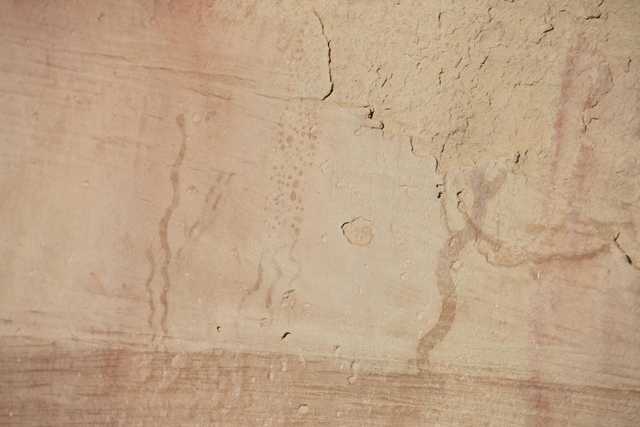 A section of a rock wall features faint markings that resemble wavy lines, as well as small circles and other indistinct shapes.